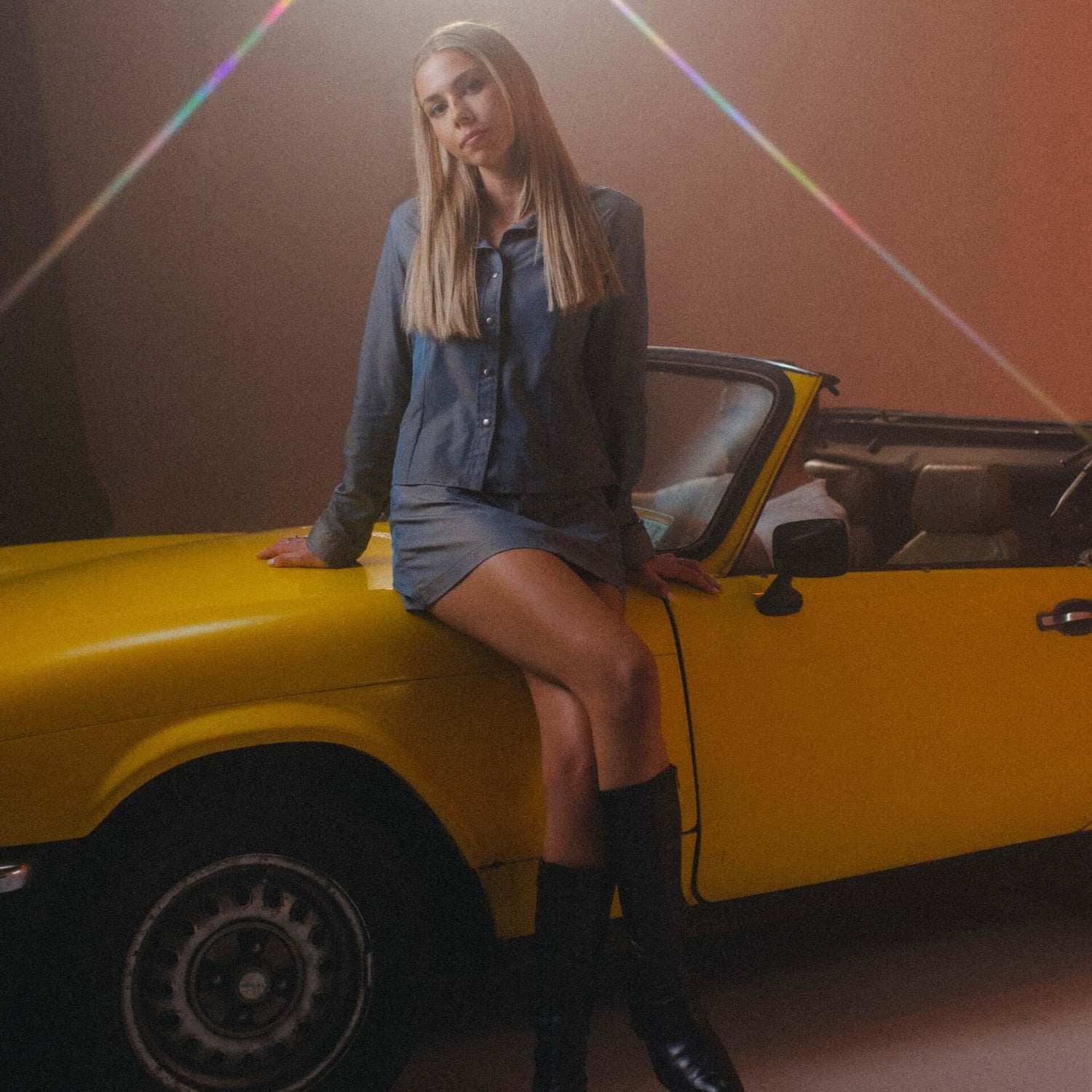 Saharaa music never leave cover art. Saharaa sitting on a yellow sports car dressed in a grey Beachbrains skirt and top